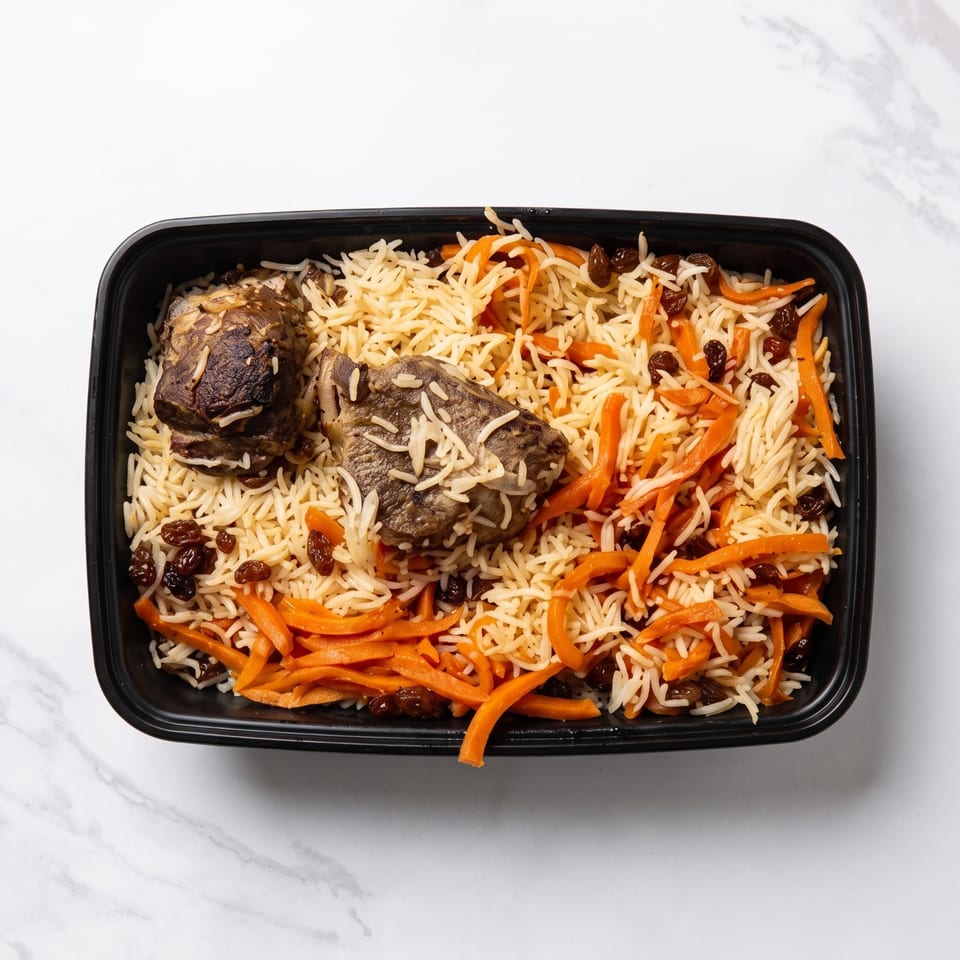 Black takeaway container filled with spiced rice, roasted meat, shredded carrots, and raisins on a marble surface.