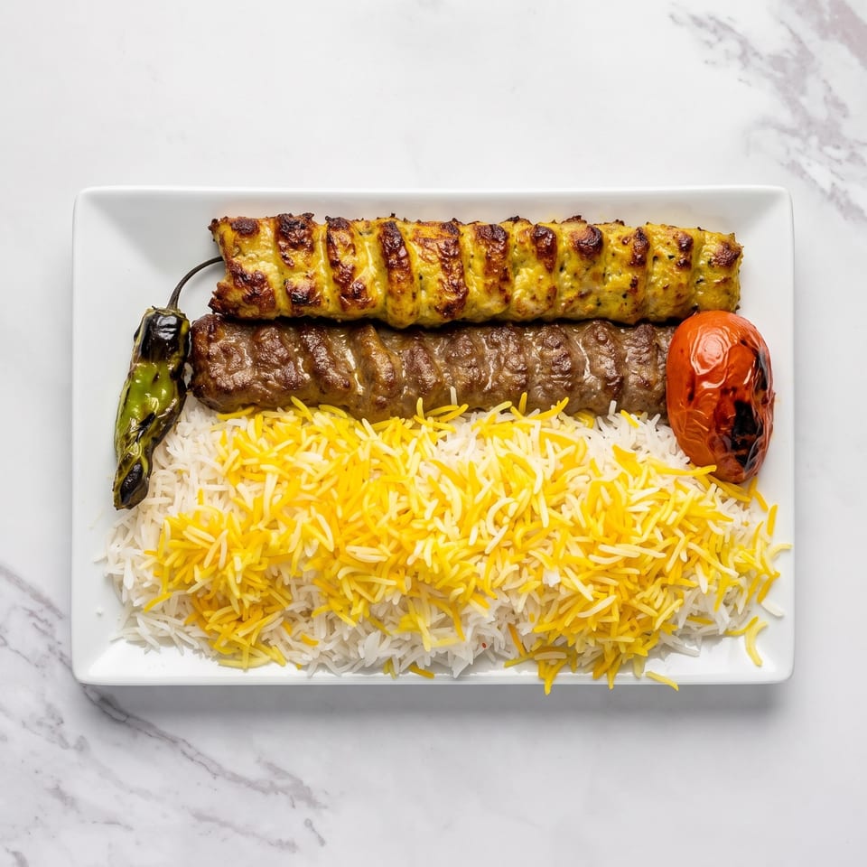 Grilled Persian kebabs served with saffron basmati rice, roasted green pepper, and tomato on a white rectangular plate.