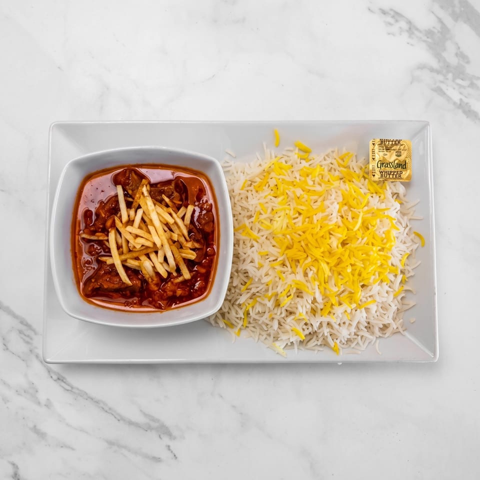 Basmati rice with saffron strands served alongside a saucy meat stew topped with French fries on a rectangular platter.